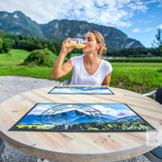 Woman drinking beer in great outdoors setting with printed counter mats on a wooden table.