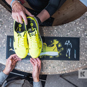 Top down view of person handing yellow trainers to clerk for sale, a desk has a branded counter mat
