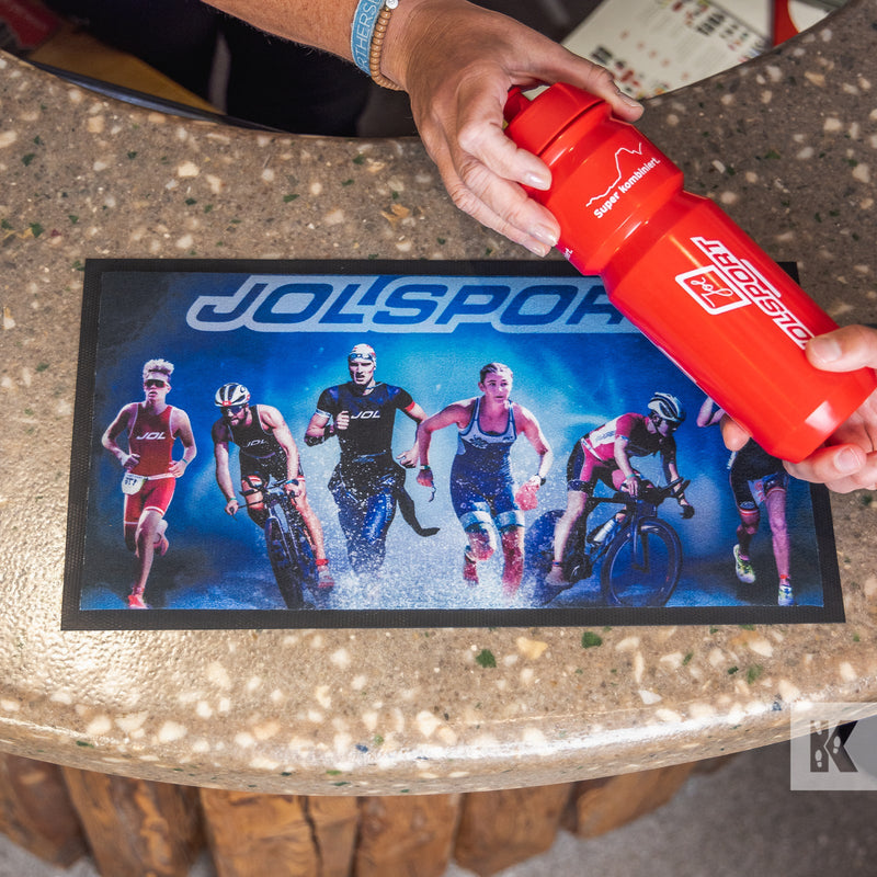 Red water bottle being passed across a high-resolution printed counter mat