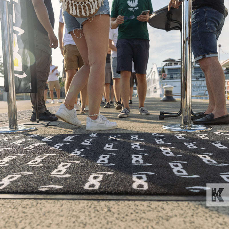 Low level view of people queuing to get on a big boat with a branded mat