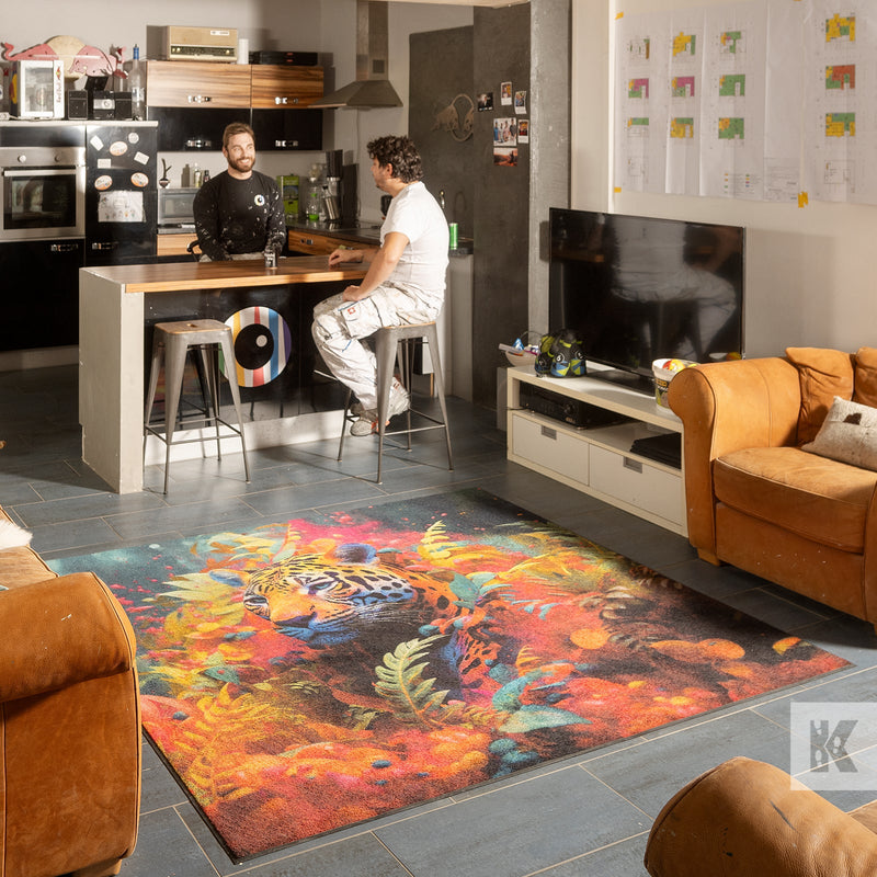Workplace scene with 2 men, centred is a large colourful mat depicting a leopard amongst colourful floral elements