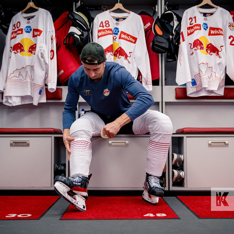 Hockey player using Sellotape to hold leg guards in place whilst sitting in changing room with numbered red mats