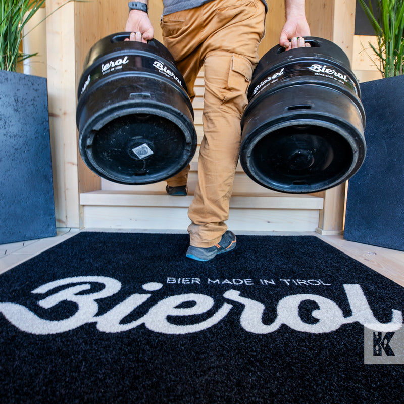 Thirsty bloke carries two kegs of beer into a building across a Bierol branded floor mat