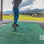 Man smashing a golf ball into the sky on a driving range with a branded T-Off mat under foot