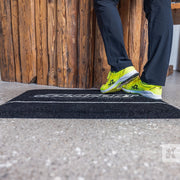 Person in dark blue trousers and bright yellow trainers stood on a Jolsport branded mat