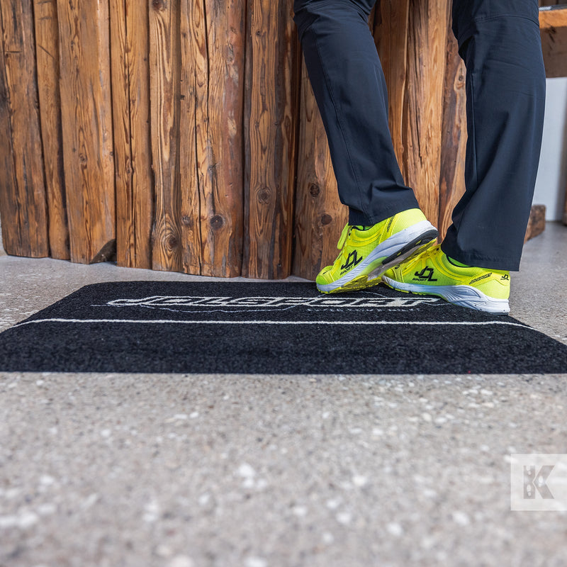 Person in dark blue trousers and bright yellow trainers stood on a Jolsport branded mat