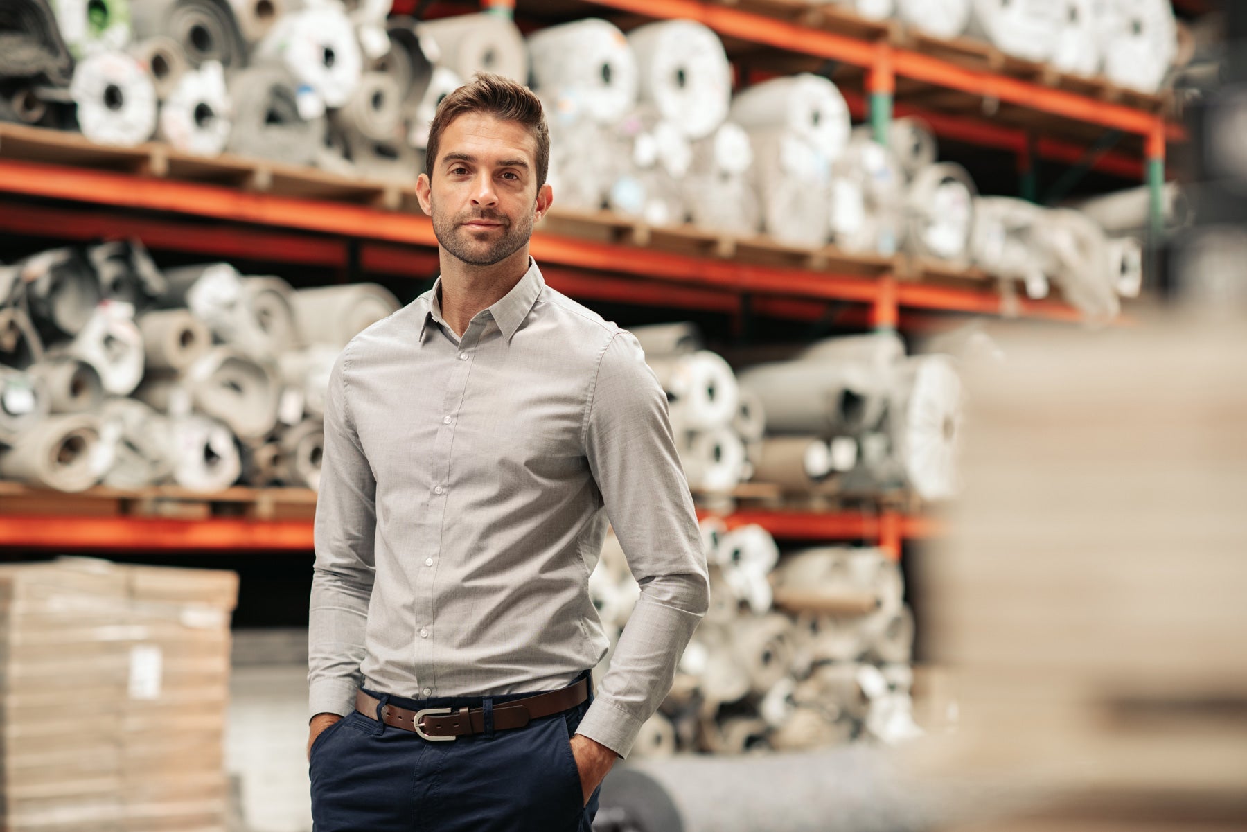 Man in warehouse standing in front of orange racking with rolls of white fabric