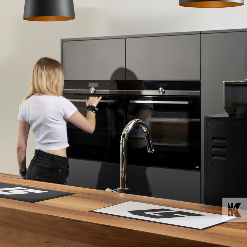 lady in kitchen using oven with a bar in foreground and bar mats