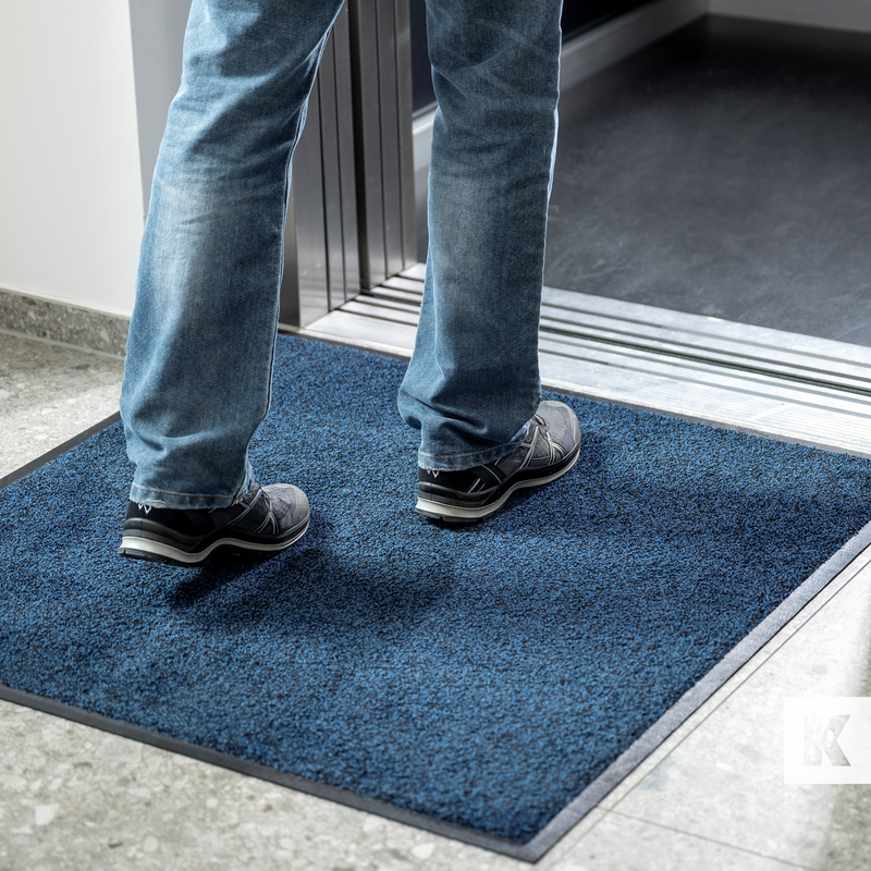 man about to enter a lift with a grey interior, standing on a blue mat
