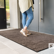 Lady about to enter a building with a grey door, standing on a brown mat