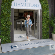 A custom logo mat printed with the name 'Hamiltons' entrance mat displayed outside a business establishment with a woman standing beside it.
