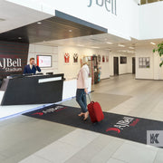 AJBell stadium reception, a lady arrives with a red suitcase on a long Jet-Print Horizon printed mat