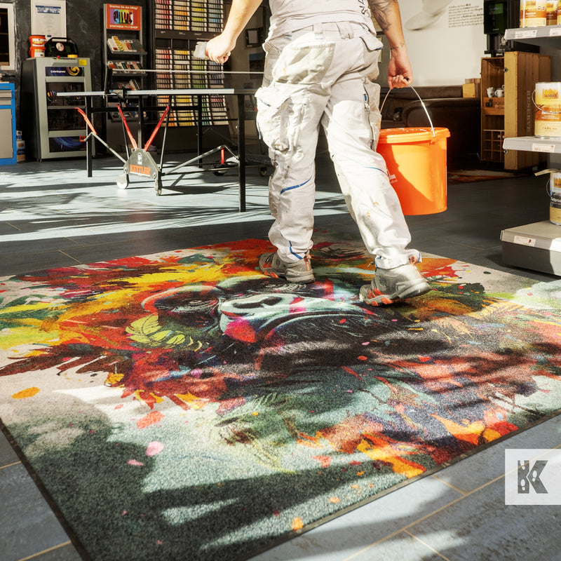 Decorator carrying bucket across a large printed mat with a colourful monkey design
