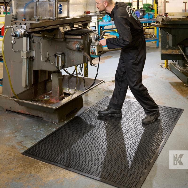 Person working on a machine in an industrial setting with a Kastor and Knavel mat.