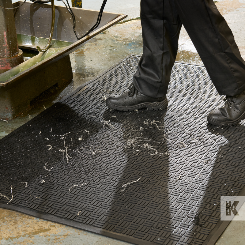 Person wearing black shoes stepping onto a textured black mat with a visible brand logo.