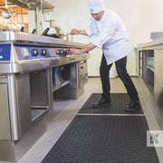 Chef adjusting a commercial kitchen cooker while standing on a Kleen-Thru Plus mat