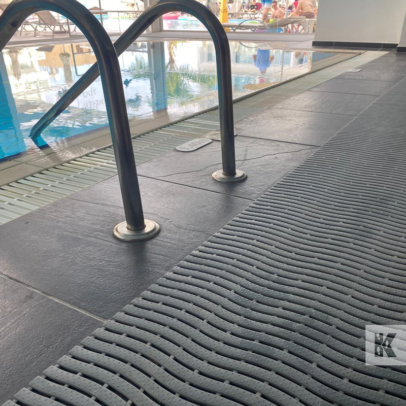 Textured black mat on a pool deck with pool equipment in the background