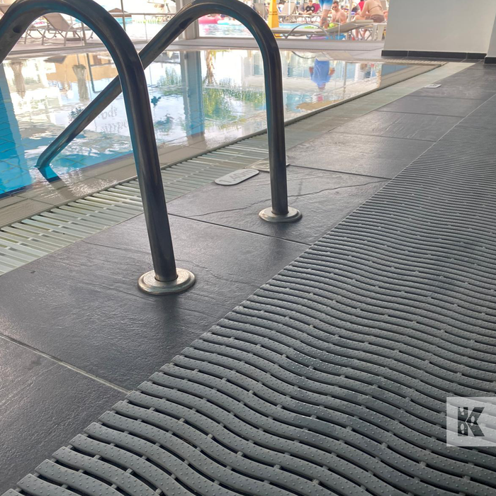Textured black mat on a pool deck with pool equipment in the background