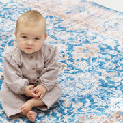 Baby in a gray outfit sitting on a blue and white patterned rug