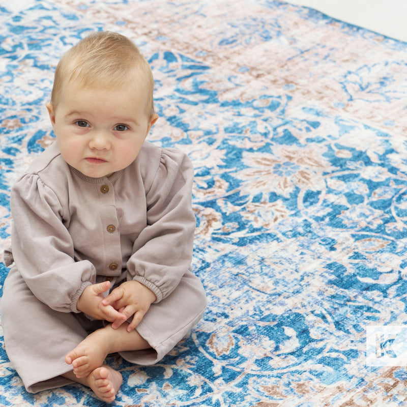 Baby in a gray outfit sitting on a blue and white patterned rug