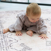 Baby in a light gray outfit sitting on a patterned rug