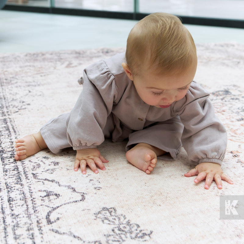 Baby in a light gray outfit sitting on a patterned rug