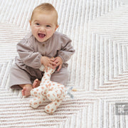 Baby in a gray outfit holding a spotted toy on a textured blanket