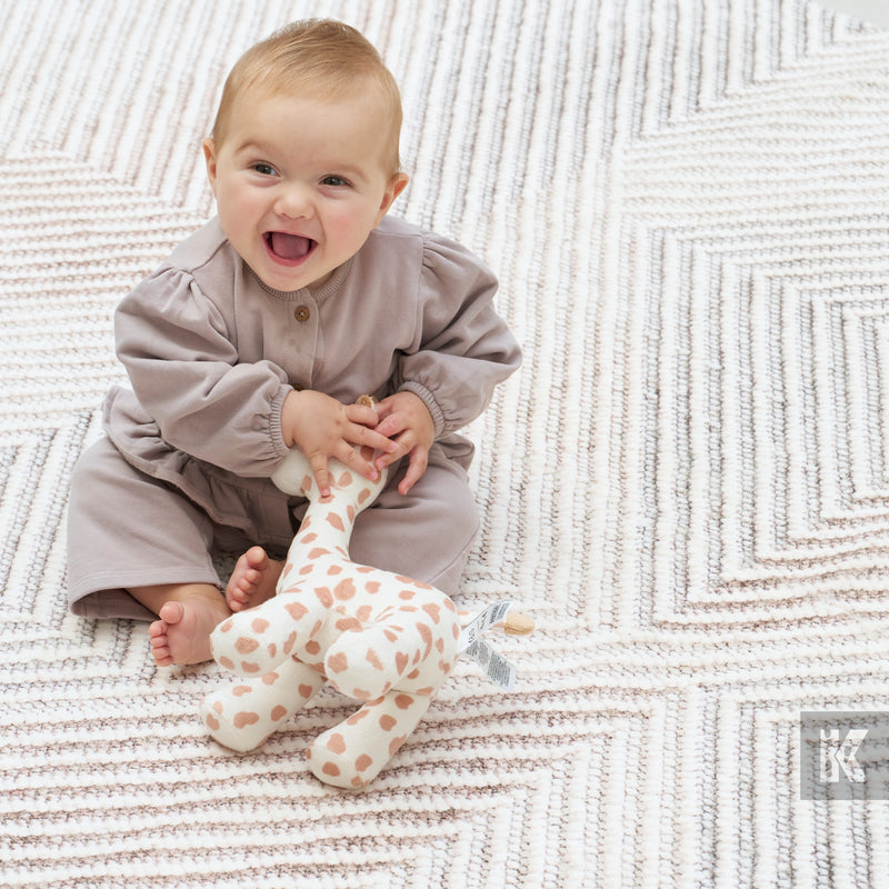 Baby in a gray outfit holding a spotted toy on a textured blanket