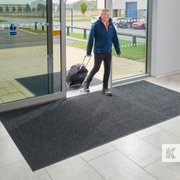 Man exiting a building with luggage on a textured mat, with 'HK' logo in the corner.
