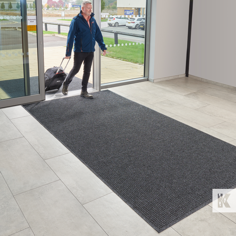 Man with a suitcase exiting a building onto a textured mat.